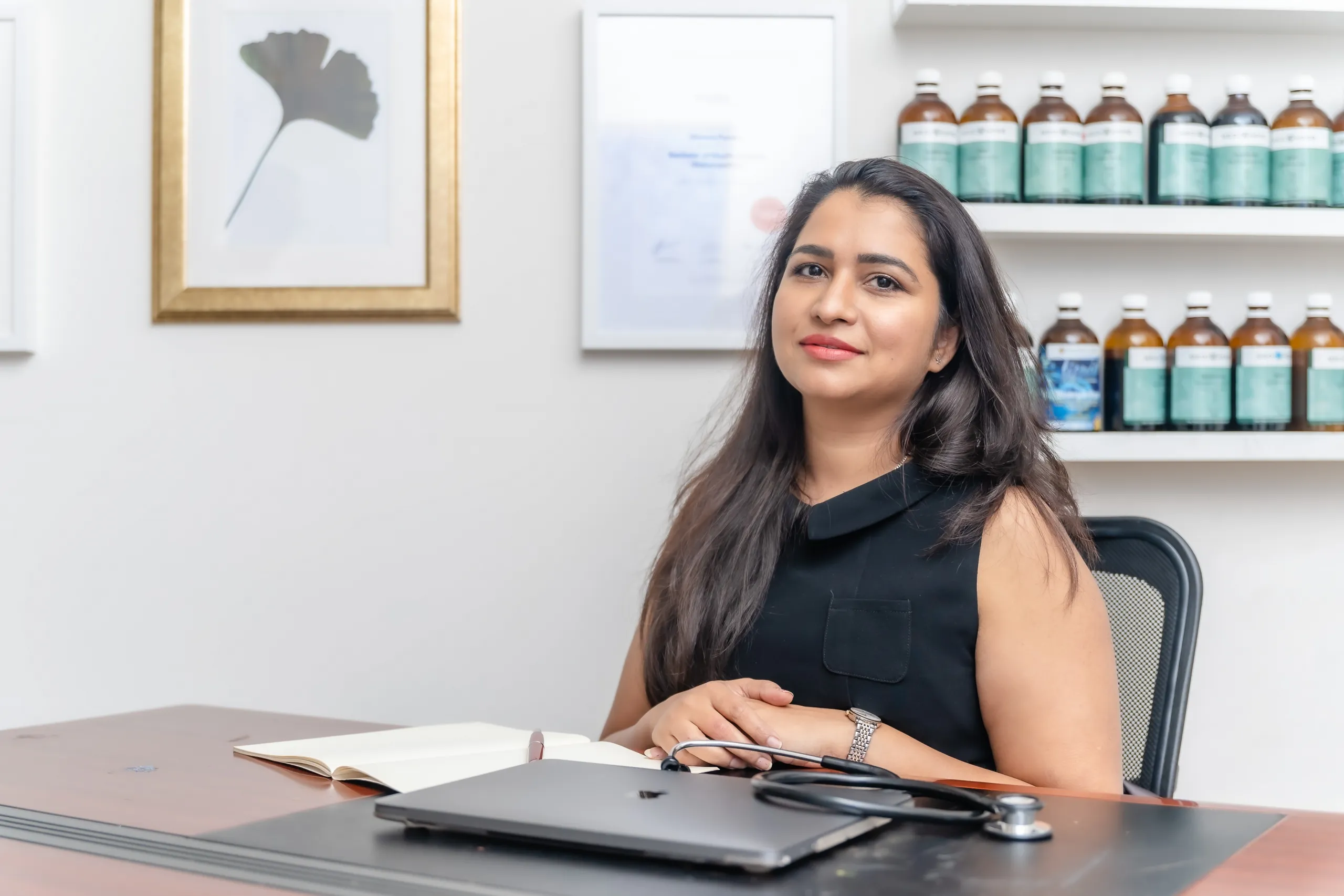 Shweta Pandey at her consulting desk, with her naturopathy degree and dispensary shelves behind her