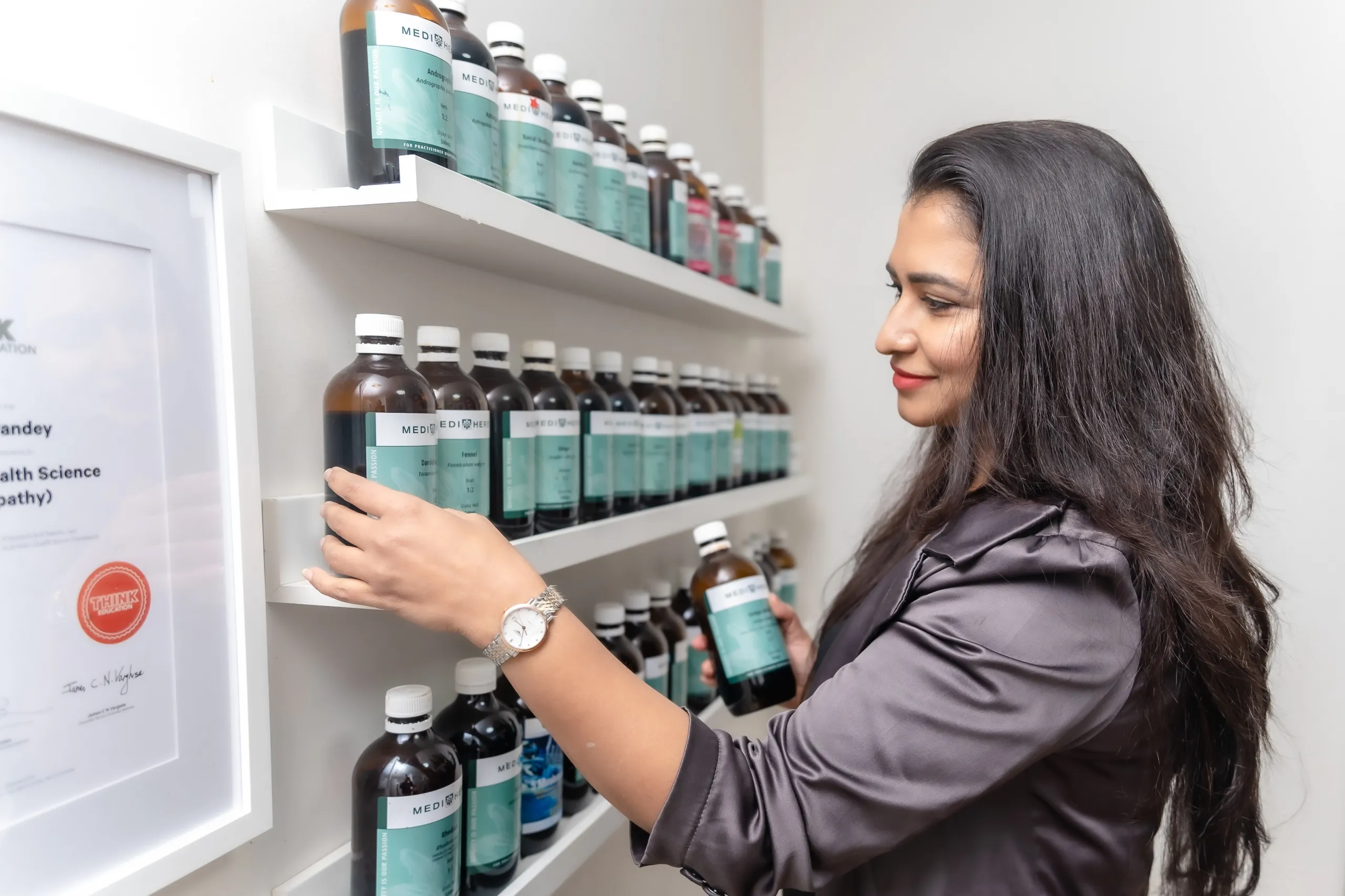 Shweta Pandey selecting a bottle of liquid herbal extract from the dispensary shelf in her Toongabbie clinic